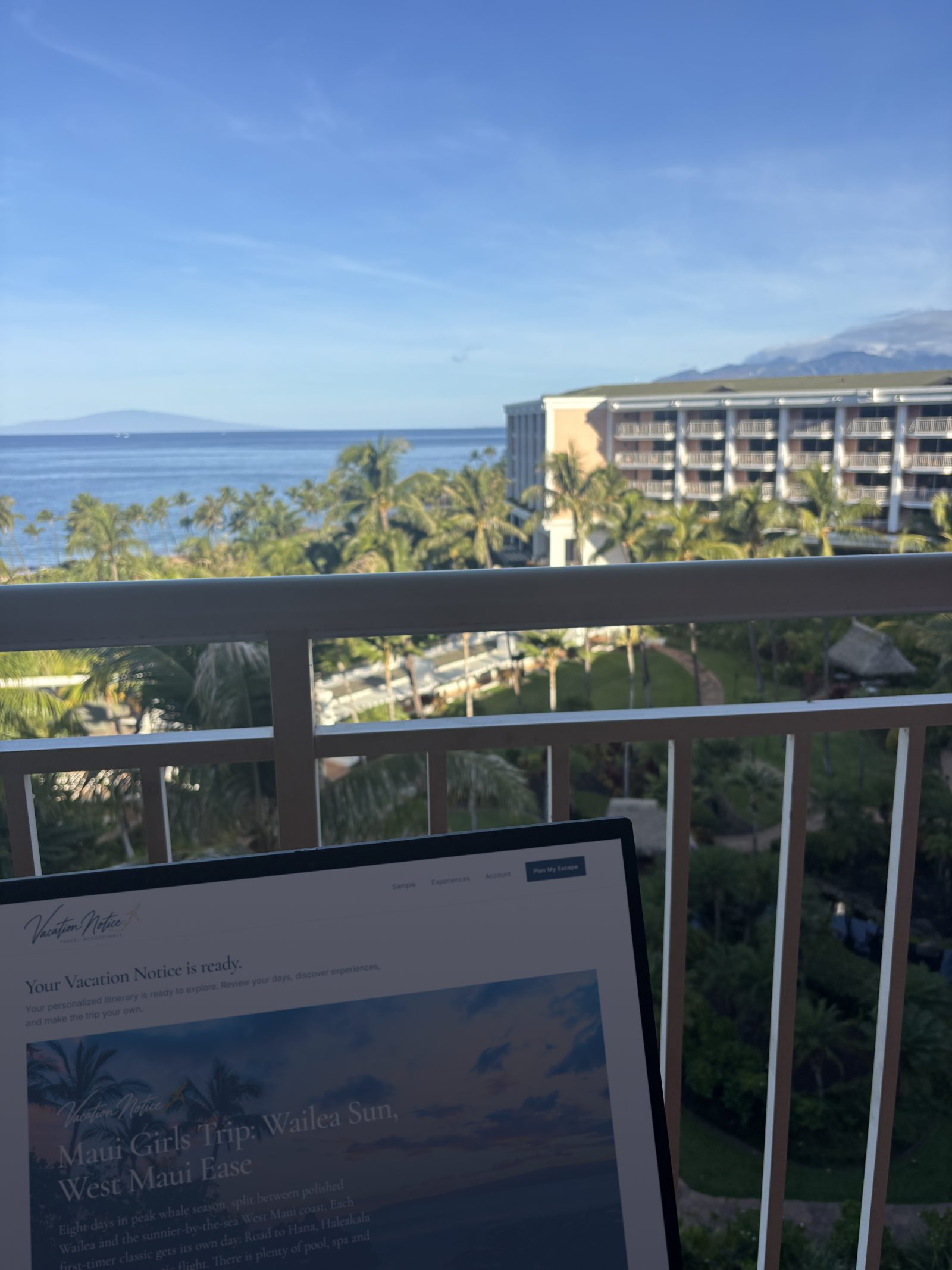 A laptop showing a Vacation Notice itinerary on a hotel balcony overlooking the ocean and palm trees at the Grand Wailea, Maui